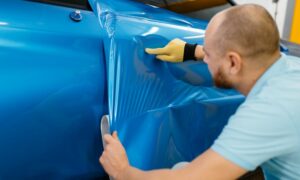 technician applying blue vinyl wrap to car for fleet leasing